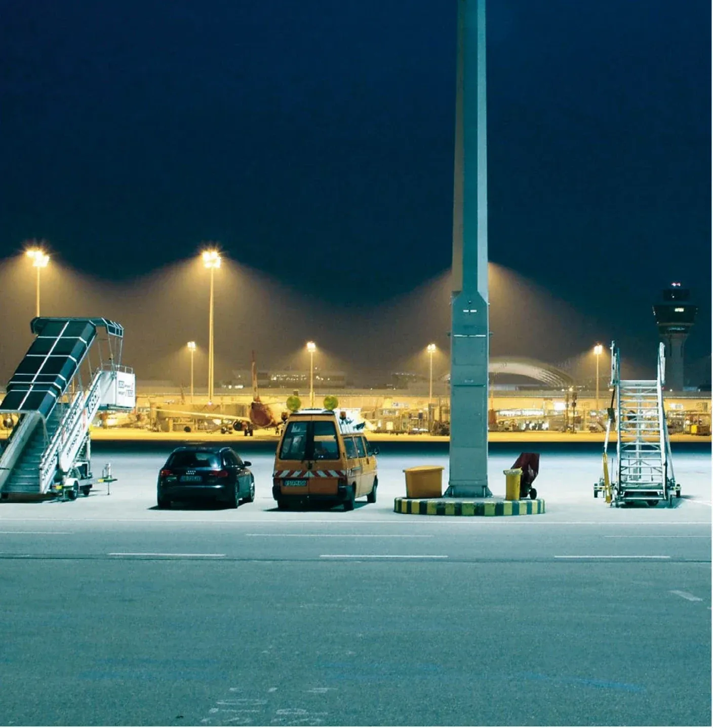 Airport apron at night with a parked aircraft, ground service vehicles and control tower